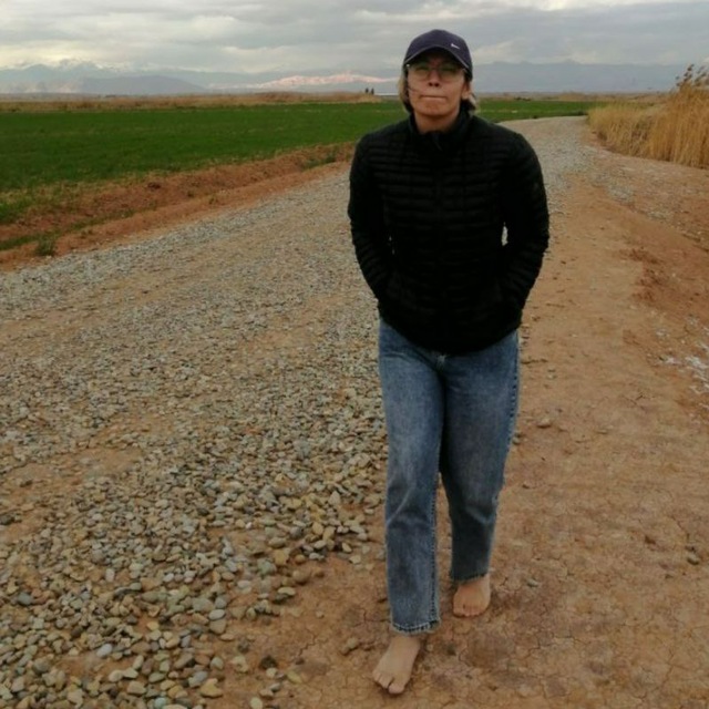 Sepideh Saied walking barefoot on a countryside path between green fields and distant mountains